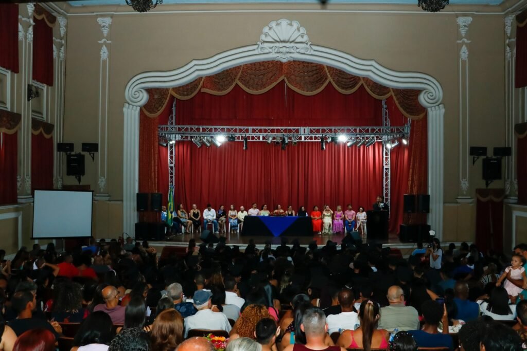 Colação de grau em teatro histórico, com a mesa de honra no palco e as famílias na plateia
