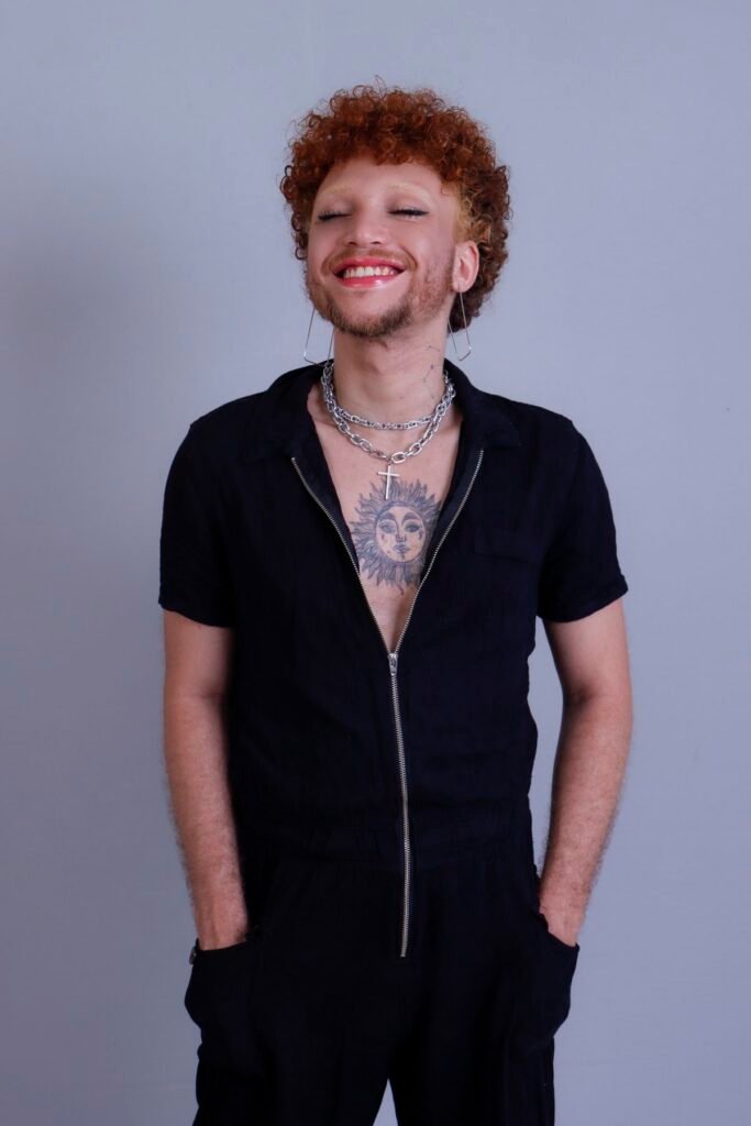 Retrato artístico sorrindo de olhos fechados, de macacão preto e correntes prateadas