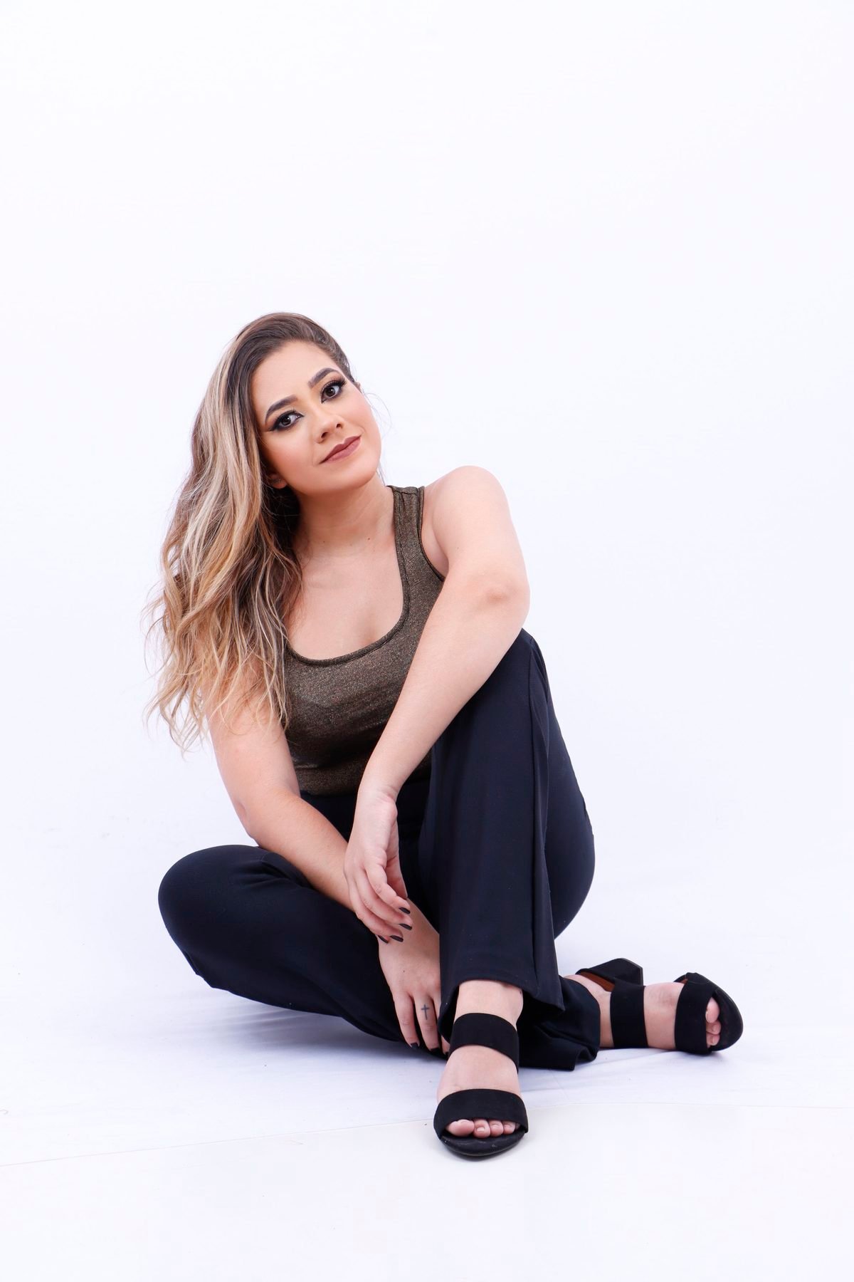 Influenciadora sentada no chão do estúdio de blusa dourada e calça preta