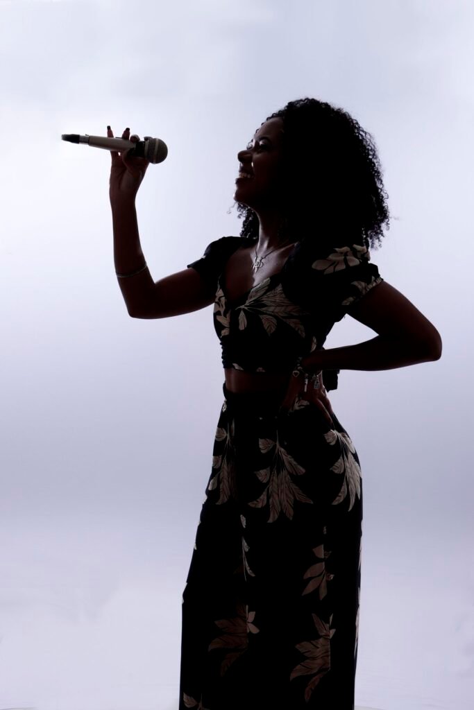 Silhueta de cantora segurando microfone contra a luz do estúdio