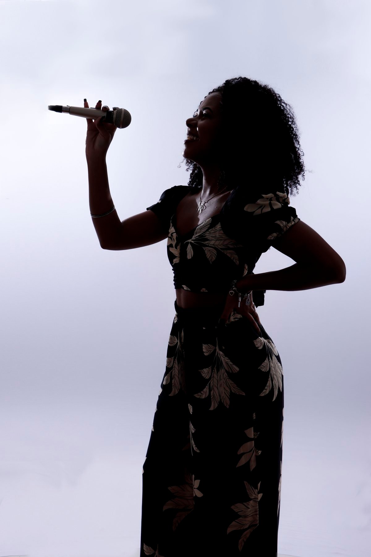Silhueta de cantora segurando microfone contra a luz do estúdio