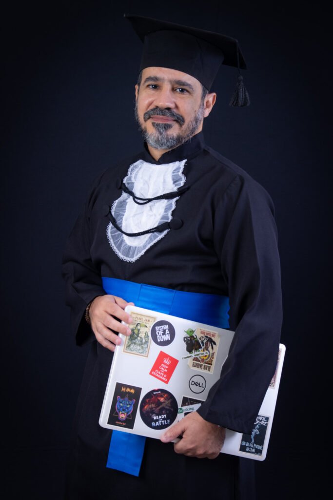 Formando de Análise e Desenvolvimento de Sistemas de beca e faixa azul segurando o notebook cheio de adesivos