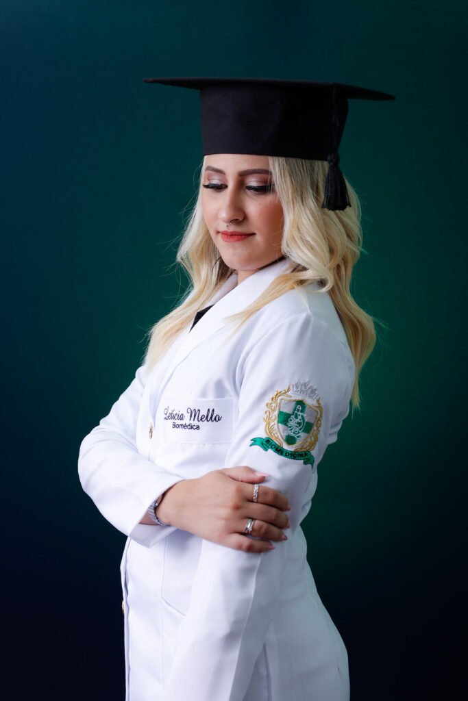 Formanda de Biomedicina de jaleco bordado e capelo, olhando para baixo no fundo verde
