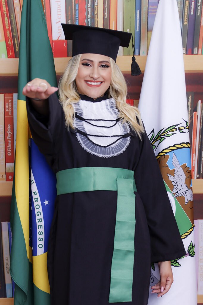 Formanda de Biomedicina fazendo o juramento entre as bandeiras do Brasil e do Rio de Janeiro, no cenário de biblioteca