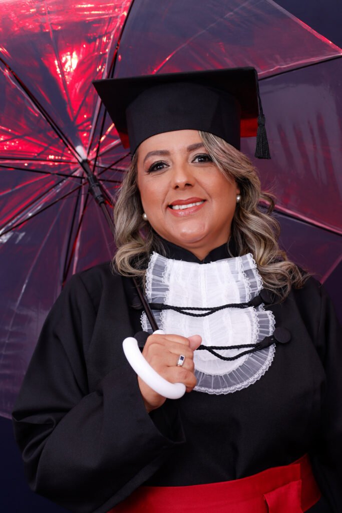 Formanda de Ciências Contábeis de beca e capelo sob um guarda-chuva transparente com luz vermelha