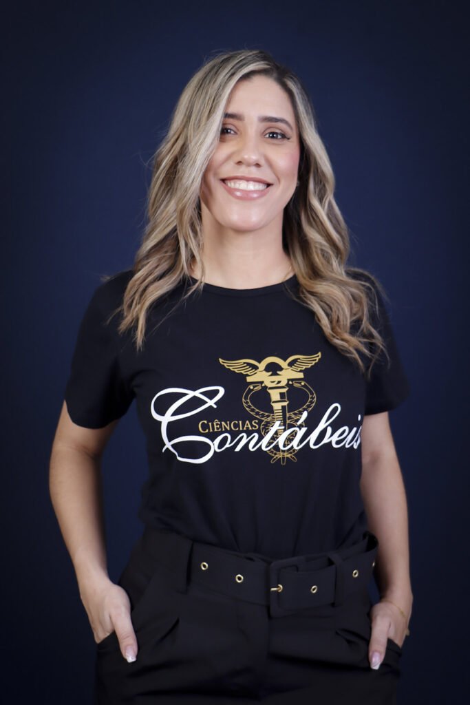 Formanda de Ciências Contábeis com a camiseta do curso, sorrindo com as mãos nos bolsos no fundo azul