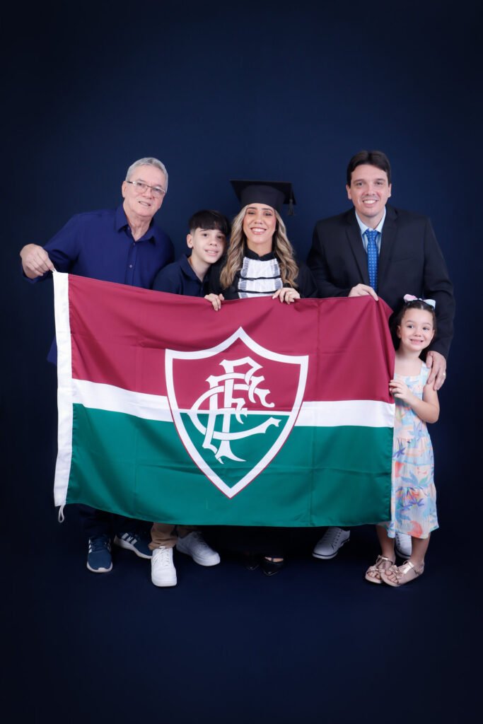 Formanda de Ciências Contábeis de beca com quatro pessoas da família segurando a bandeira do time do coração