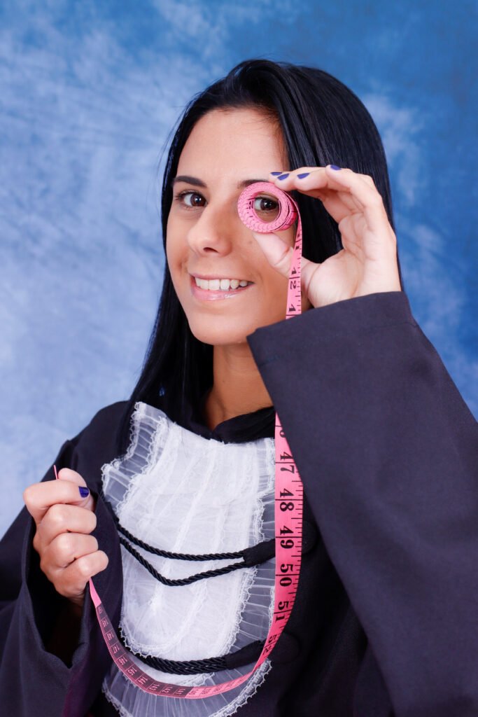 Formanda de Design de Moda de beca olhando através de uma fita métrica rosa enrolada
