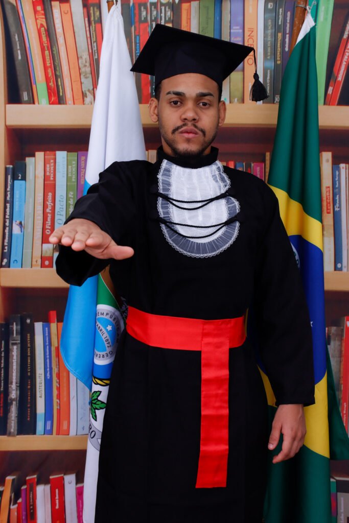 Formando de Direito de beca e faixa vermelha fazendo o juramento entre as bandeiras do Rio de Janeiro e do Brasil, no cenário de biblioteca
