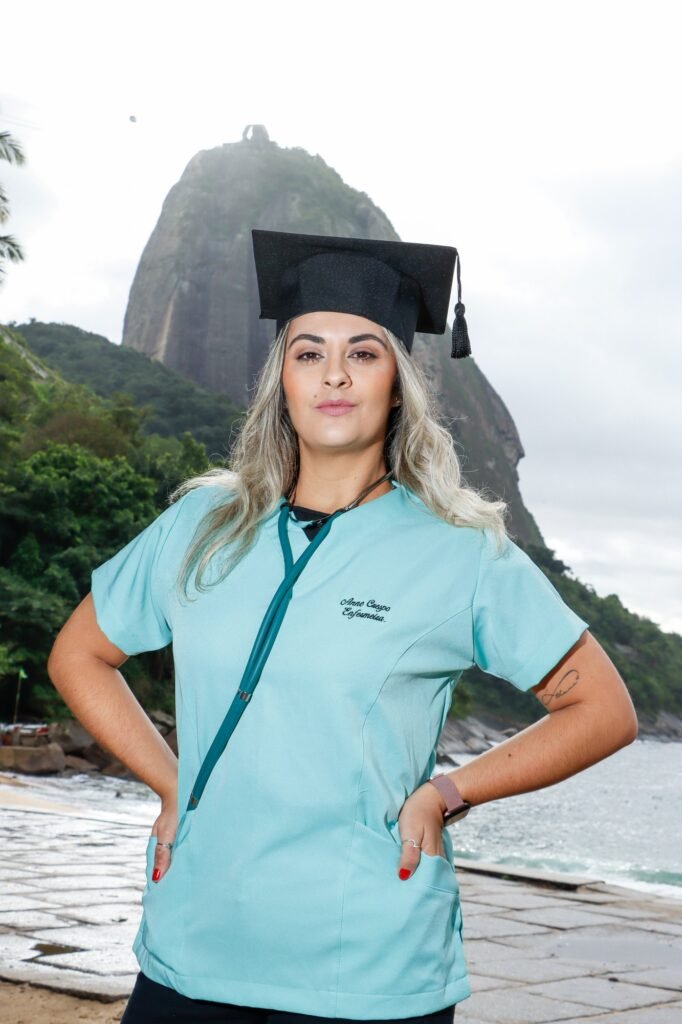 Formanda de Enfermagem de pijama cirúrgico, estetoscópio e capelo na Praia Vermelha, na Urca, com o Pão de Açúcar ao fundo