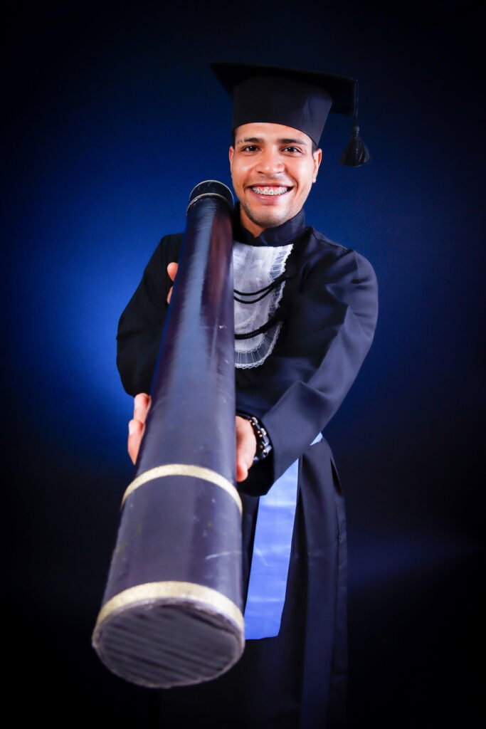 Formando do ensino médio de beca apontando um canudo gigante para a câmera