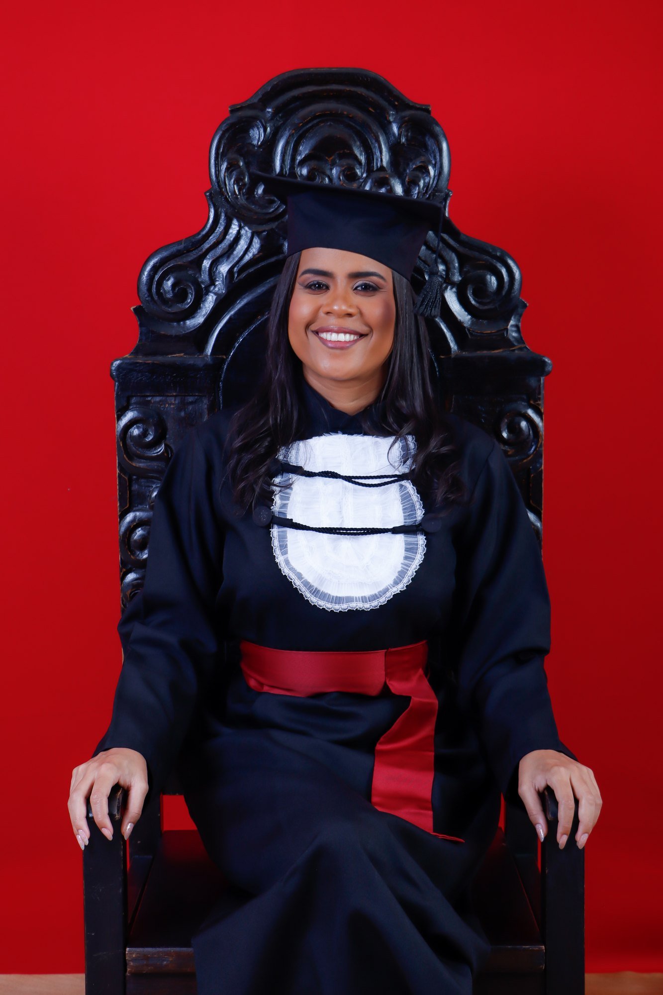 Formanda de Ciências Contábeis de faixa vermelha sentada na Cadeira Colonial Luiz XV, com fundo vermelho no estúdio do Z7 Studio