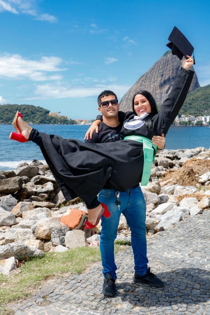 Formanda de Análises Clínicas carregada no colo, erguendo o capelo, com o Pão de Açúcar ao fundo