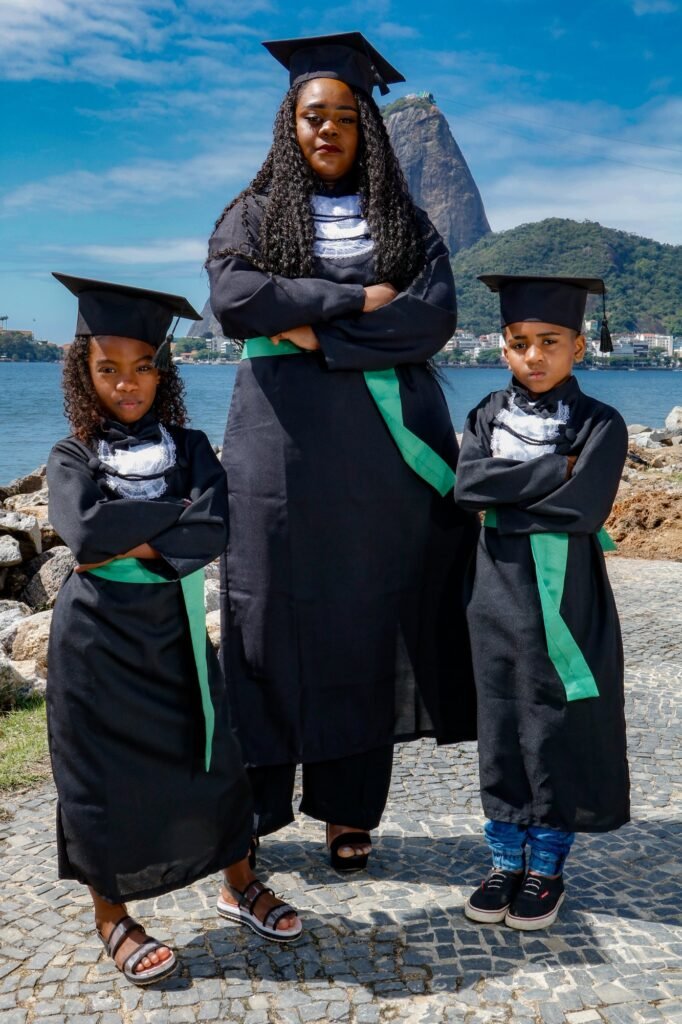 Formanda de Análises Clínicas de beca e faixa verde de braços cruzados com os dois filhos, também de beca e capelo, com o Pão de Açúcar ao fundo