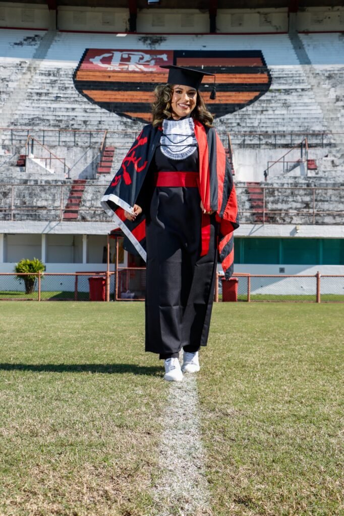 Formanda de Ciências Contábeis com a bandeira do Flamengo nos ombros, caminhando no gramado de um estádio do clube