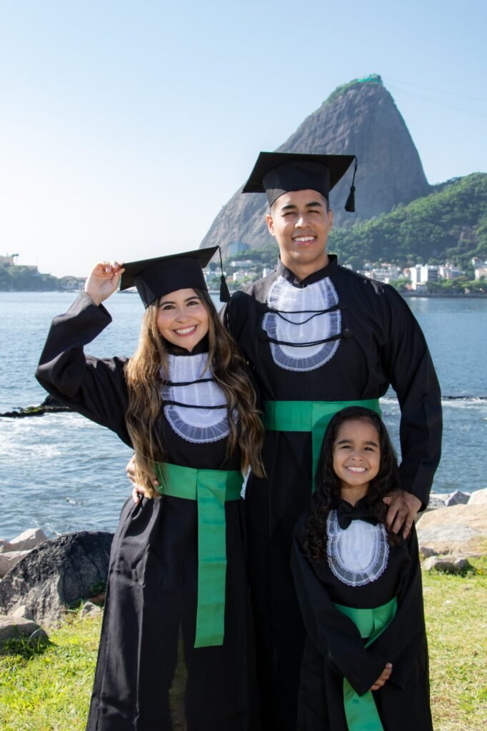 Casal de formandos de Educação Física com a filha também de beca, à beira da baía com o Pão de Açúcar ao fundo