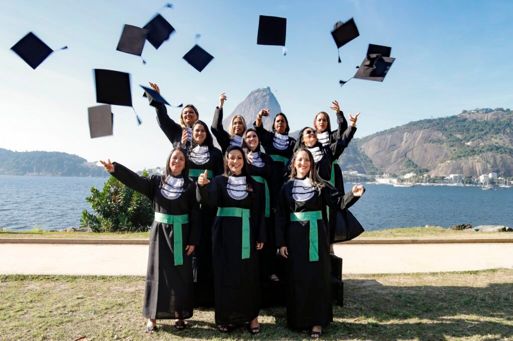 Turma de Estética e Cosmetologia de beca e faixa verde jogando os capelos para o alto, com o Pão de Açúcar ao fundo