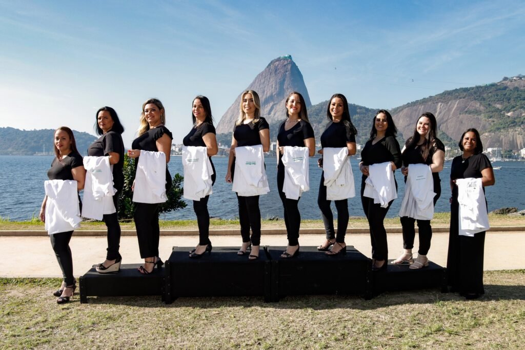 Turma de Estética e Cosmetologia de roupa preta segurando os jalecos dobrados, em fila sobre os praticáveis, com o Pão de Açúcar ao fundo