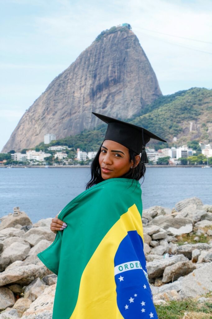 Formanda de Enfermagem com a bandeira do Brasil nos ombros, olhando para a câmera, com o Pão de Açúcar ao fundo