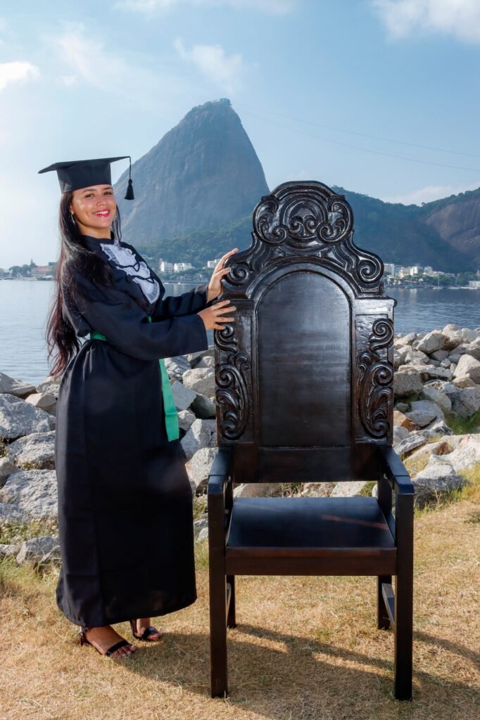 Formanda de Enfermagem de beca e faixa verde ao lado da Cadeira Colonial Luiz XV, à beira da baía com o Pão de Açúcar