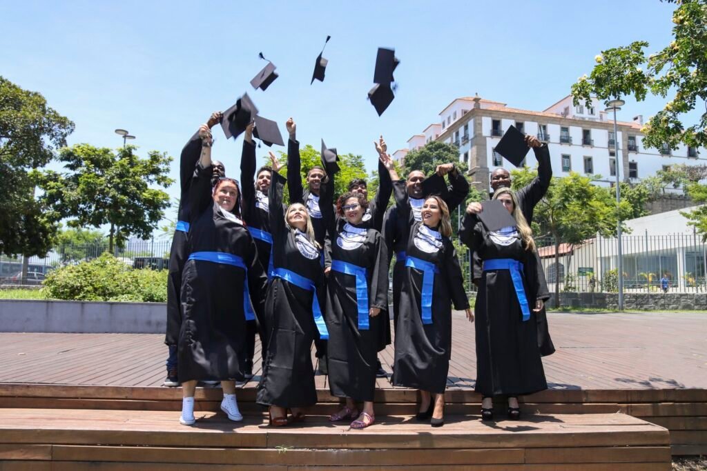 Turma de formandos de beca e faixa azul jogando o capelo para o alto em ensaio de formatura externo