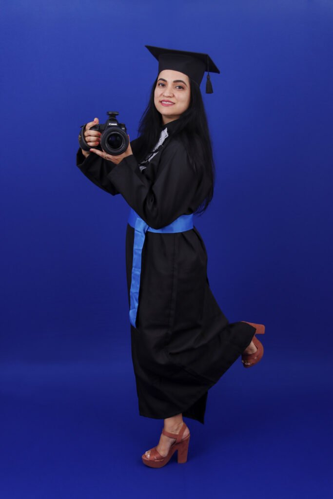 Formanda de Fotografia de beca segurando a câmera e levantando o pé, no fundo azul