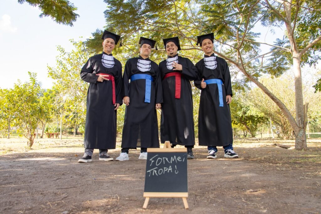 Quatro amigos de beca, com faixas vermelha e azul, atrás de um quadro escrito FORMEI TROPA, no Parque do Gericinó, em Nilópolis