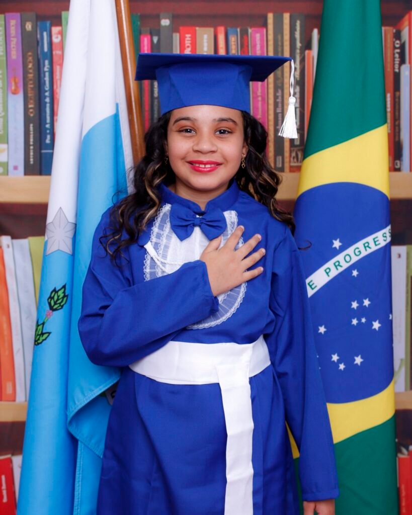 Menina de beca azul com a mão no peito entre as bandeiras do Brasil e do estado do Rio