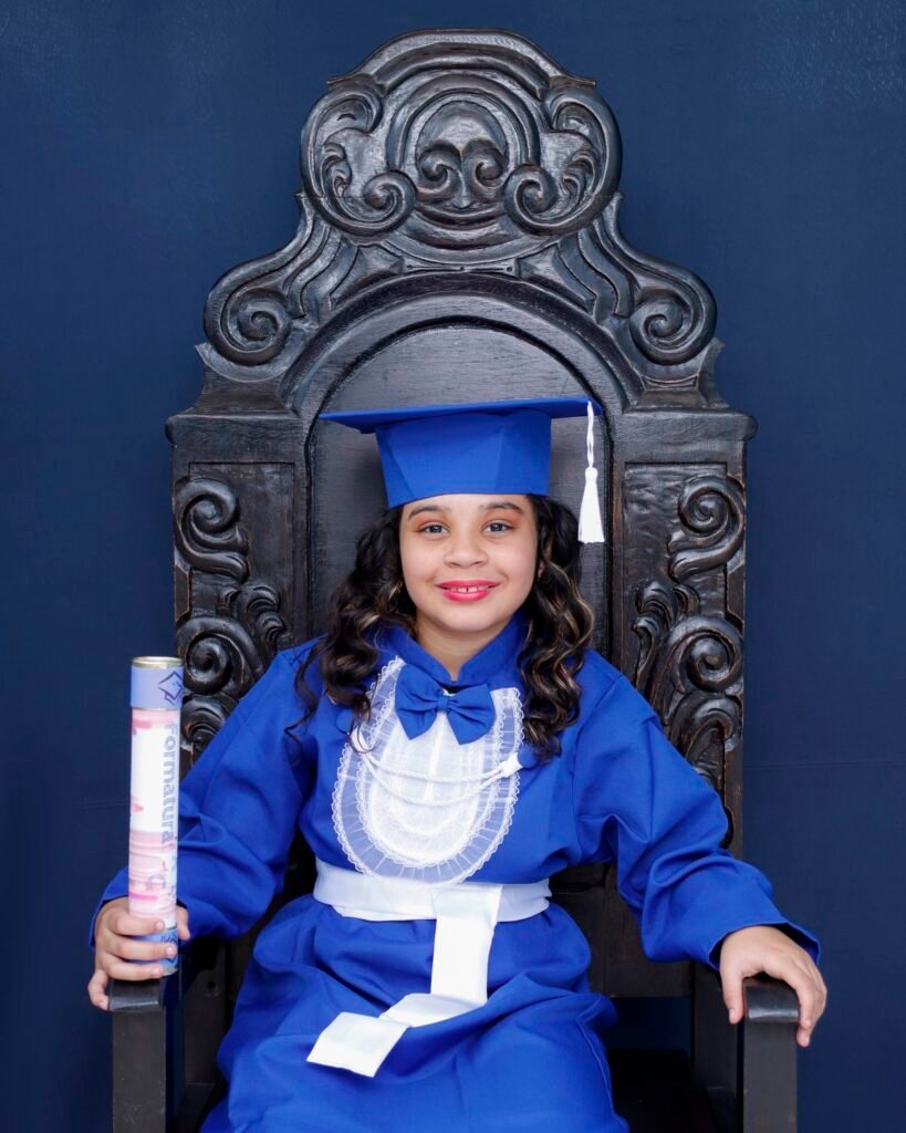 Menina de beca azul sentada na cadeira entalhada com o canudo