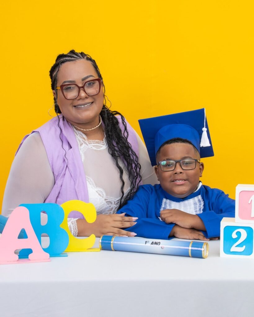 Mãe e filho de beca azul no cenário amarelo do ensaio infantil