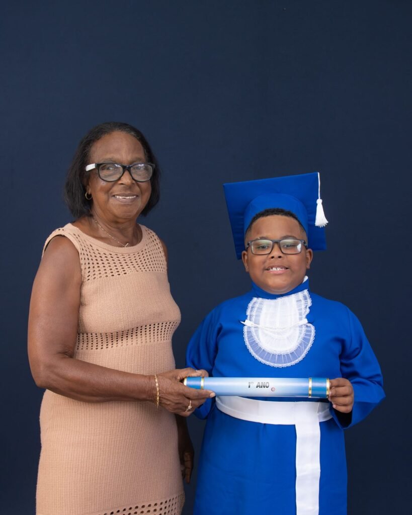 Avó e neto de beca azul segurando juntos o canudo do 1º ano