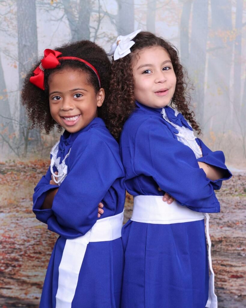 Duas amigas de beca azul posando de costas uma para a outra no cenário de floresta
