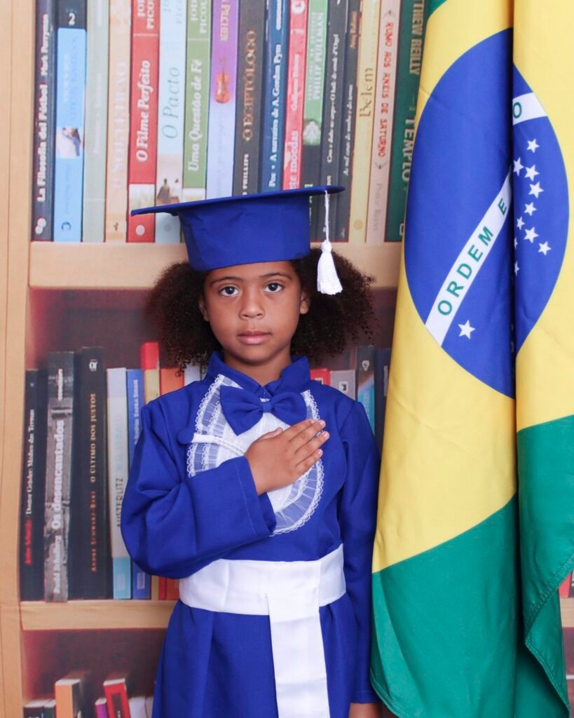 Menina de beca azul com a mão no peito ao lado da bandeira do Brasil
