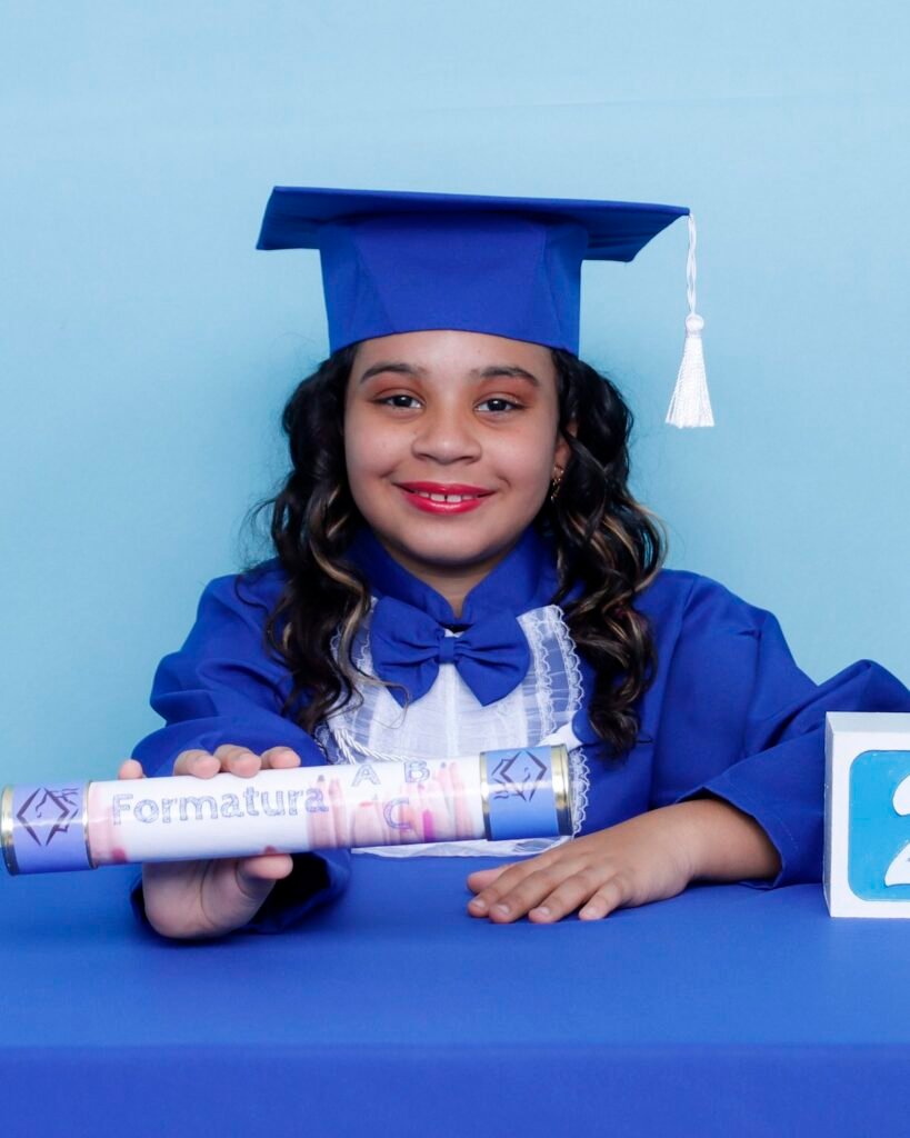 Menina de beca azul na mesa com letras ABC mostrando o canudo da Formatura ABC