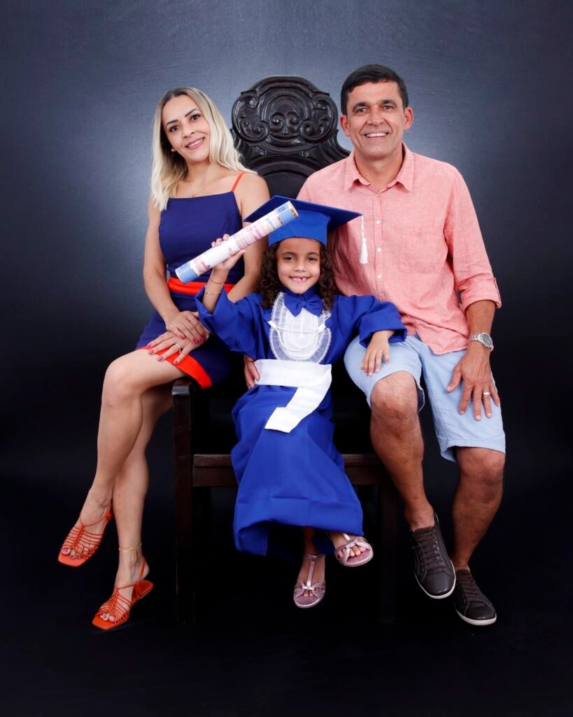 Pais e filha de beca azul na cadeira entalhada, com o canudo erguido