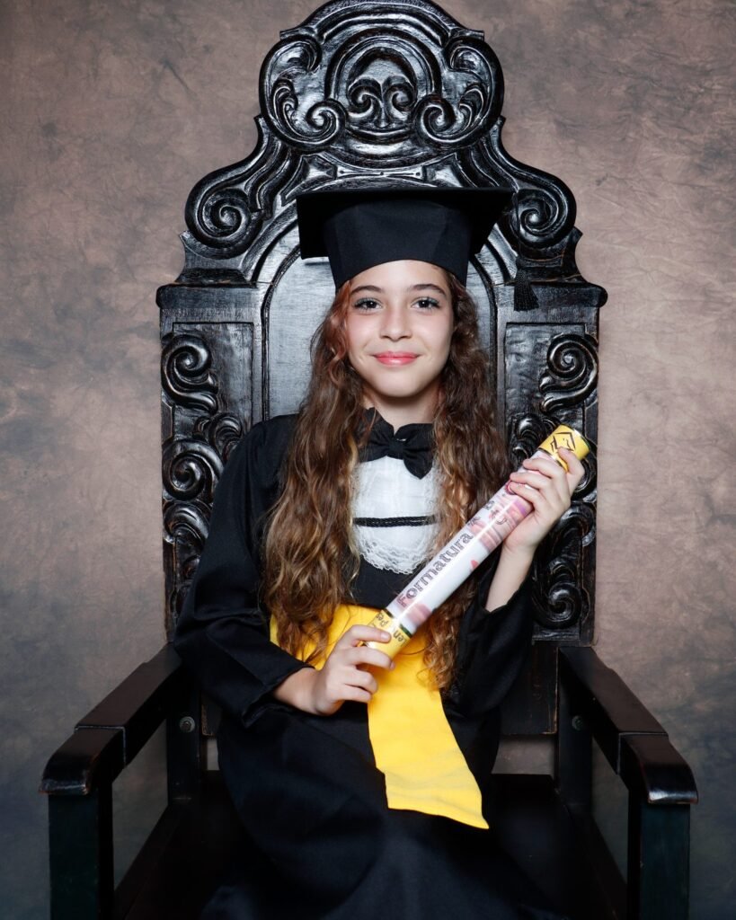 Menina de beca preta sentada na cadeira entalhada com o canudo da Formatura ABC
