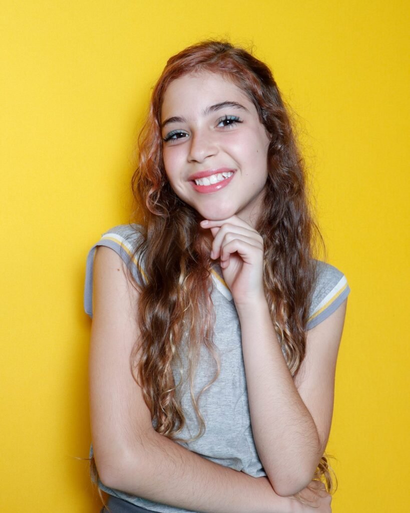 Menina sorrindo com a mão no queixo no fundo amarelo do estúdio