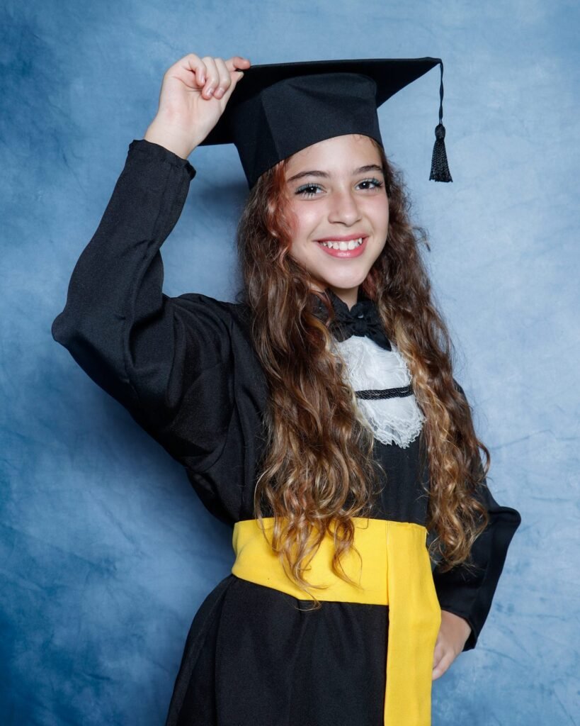 Menina de beca preta e faixa amarela segurando o capelo