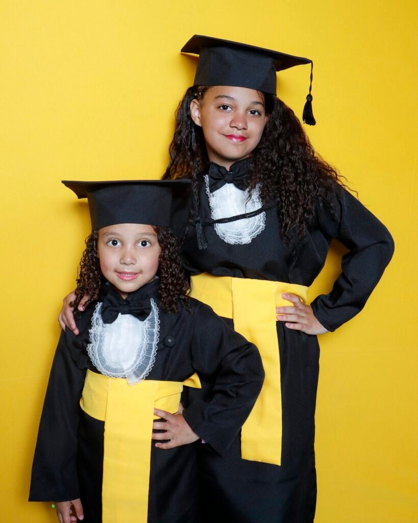 Irmãs de beca preta e faixa amarela posando juntas no fundo amarelo