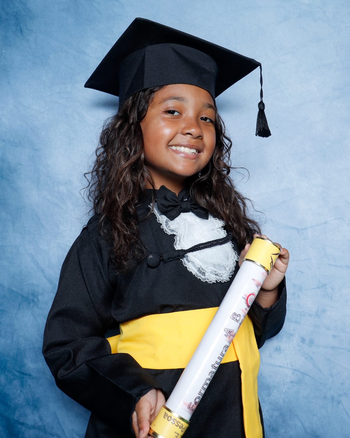 Menina de beca preta sorrindo com o canudo da Formatura ABC
