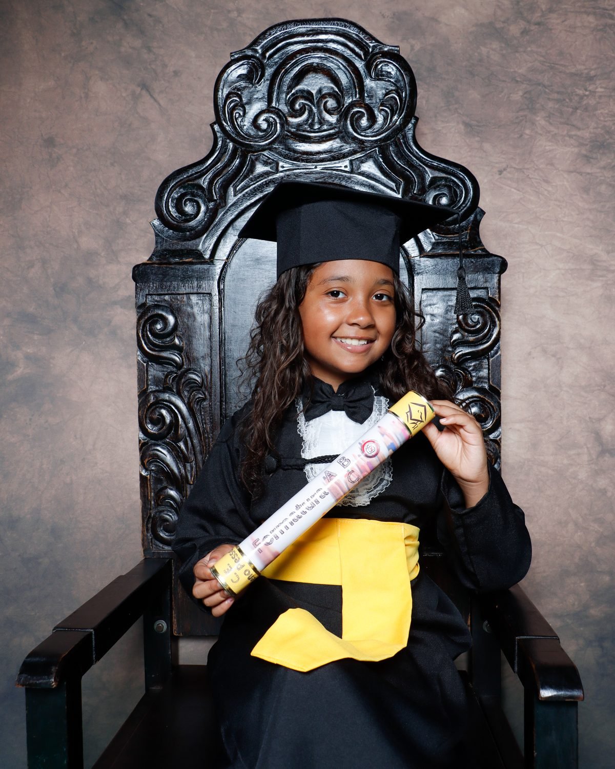 Menina de beca preta sentada na Cadeira Colonial Luiz XV com o canudo no ensaio de formatura infantil