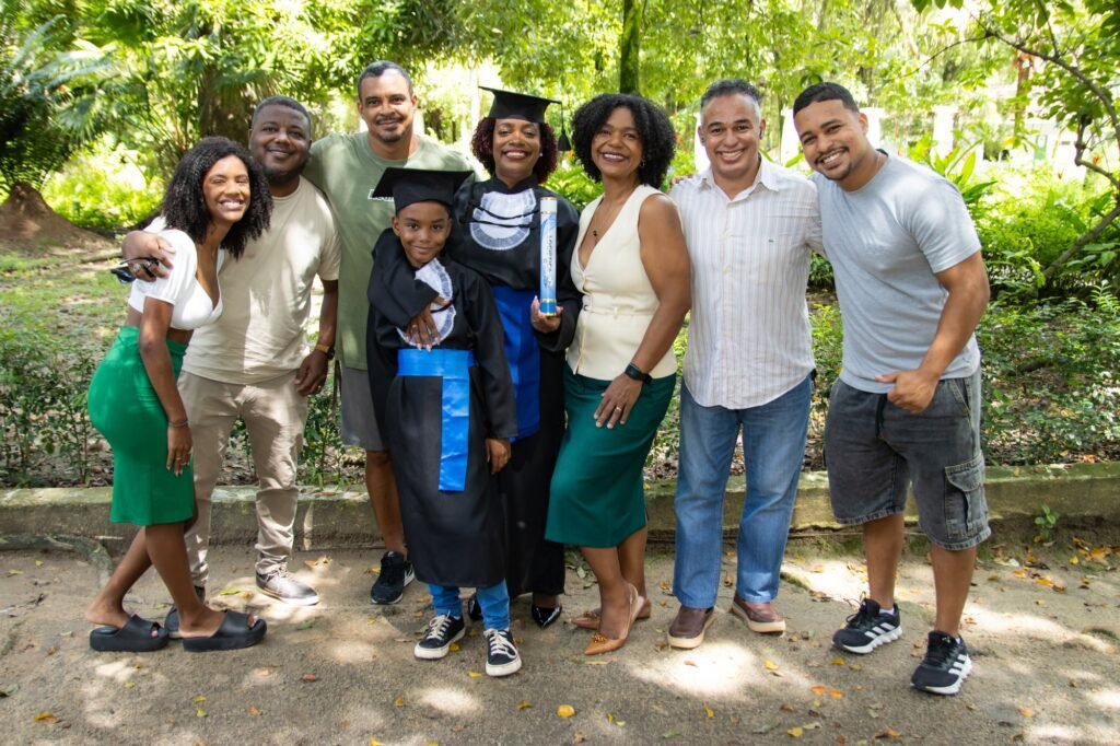Formanda de Logística do Senac com a família e o filho de beca no jardim da Fazendinha