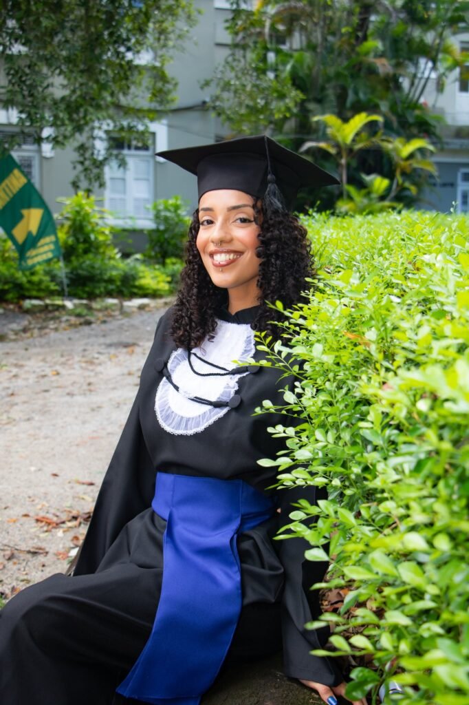 Formanda de Logística do Senac sorrindo sentada junto a uma cerca viva no jardim da Fazendinha