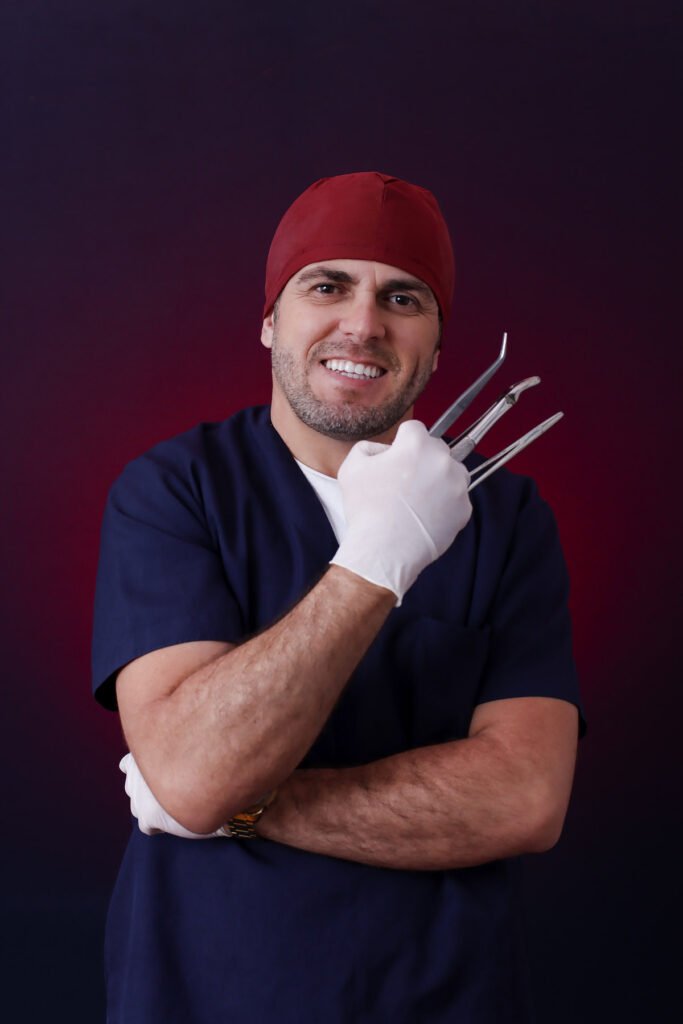 Formando de Odontologia de pijama cirúrgico, touca e luvas segurando instrumentos odontológicos, de braços cruzados