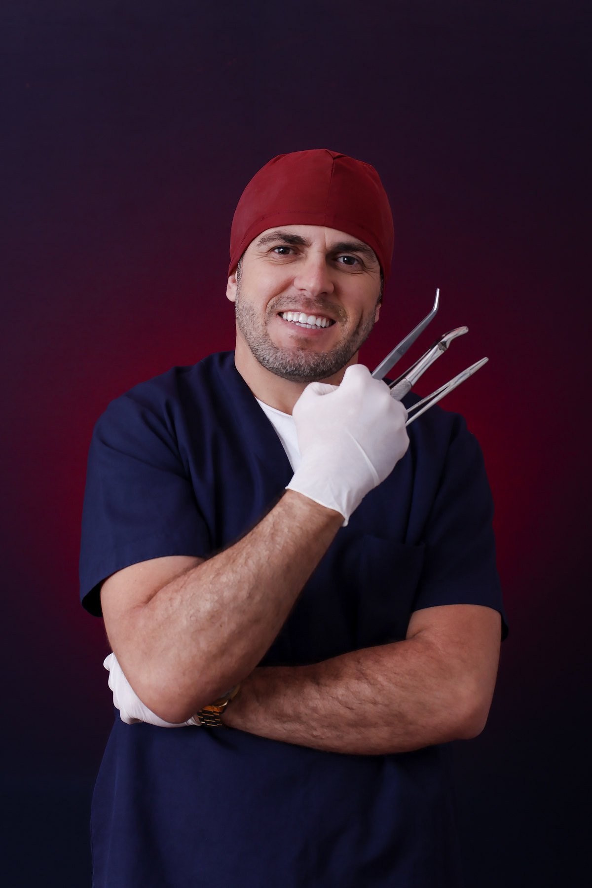 Formando de Odontologia de pijama cirúrgico, touca e luvas segurando instrumentos odontológicos, de braços cruzados