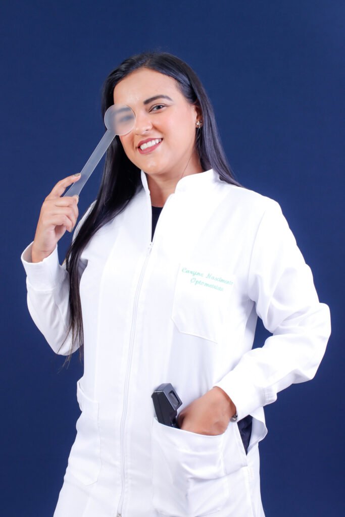 Formanda de Optometria de jaleco bordado segurando o oclusor na frente do olho, com um aparelho no bolso, no fundo azul