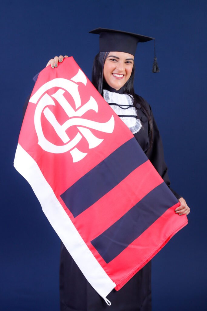 Formanda de Optometria de beca e capelo segurando a bandeira do time do coração