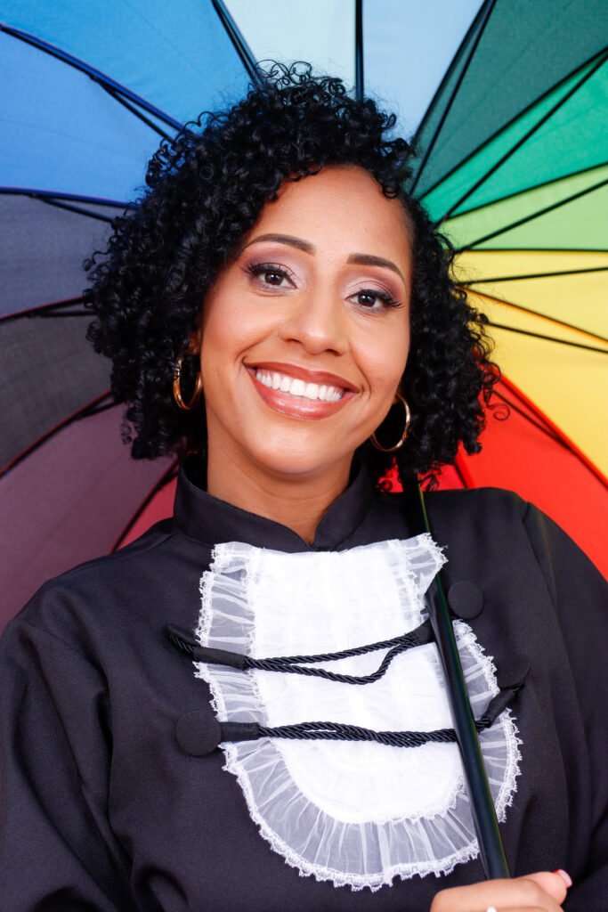 Formanda de beca sorrindo sob um guarda-chuva colorido