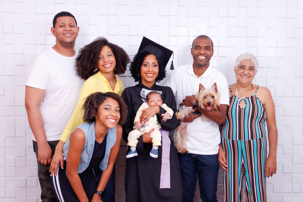 Formanda de beca e capelo com o bebê no colo, ao lado da família e do cachorro