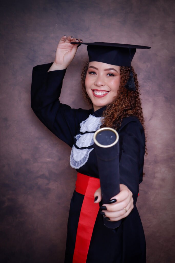 Formanda de beca segurando o capelo e estendendo o canudo para a câmera no fundo marrom